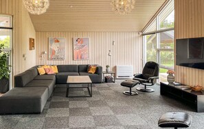 Ein modernes Wohnzimmer mit einer Eckcouch, einem Couchtisch, einem schwarzen Ledersessel und einem Fernseher an der Wand.
