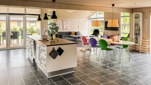 Una cocina moderna con una isla central, comedor con sillas de colores y ventanas amplias.