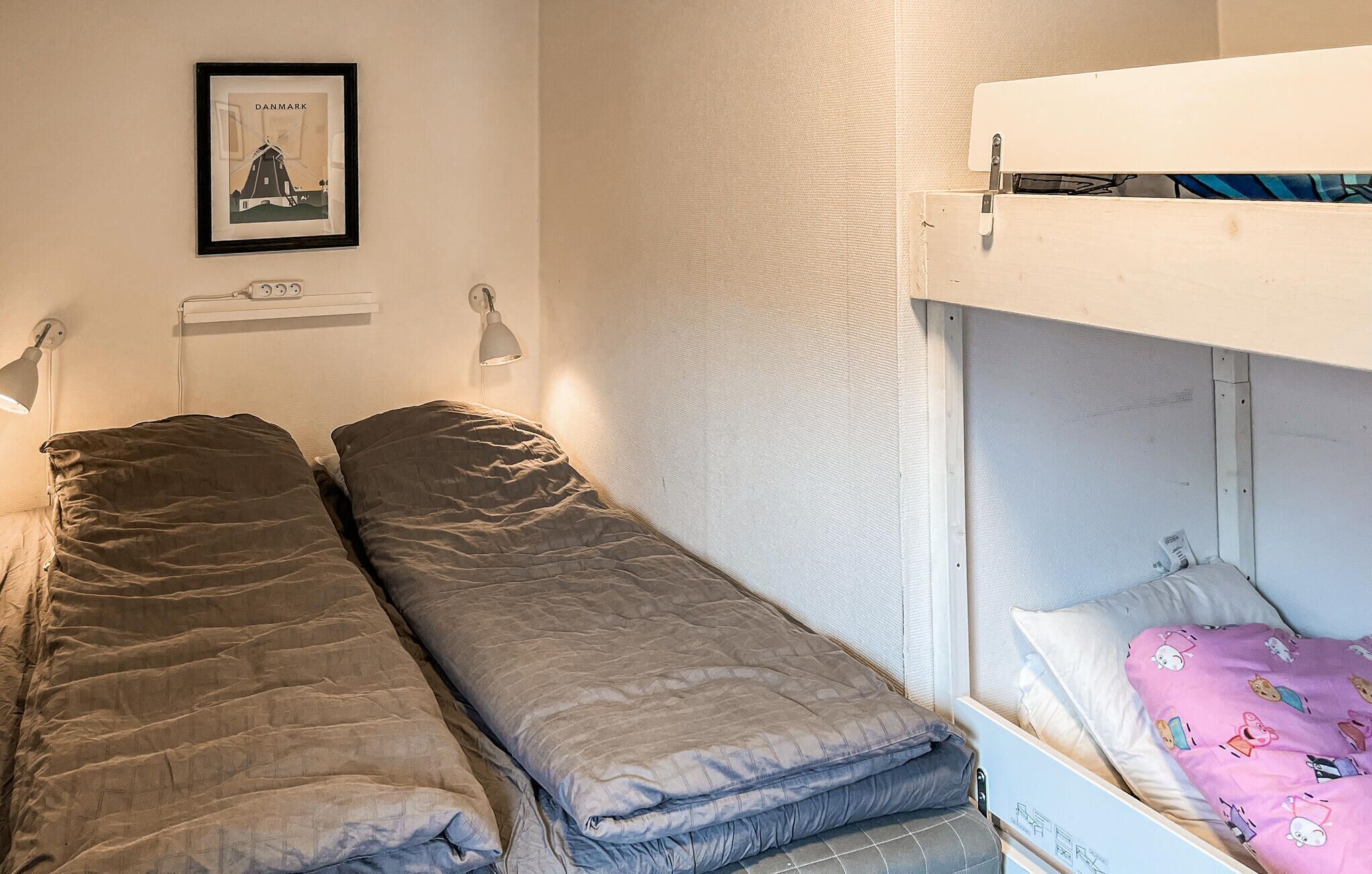 A dormitory room with bunk beds, a framed picture on the wall, and two bedside lamps.