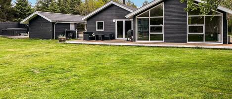 A modern building with a large glass entrance, a patio area, and a well-maintained lawn.