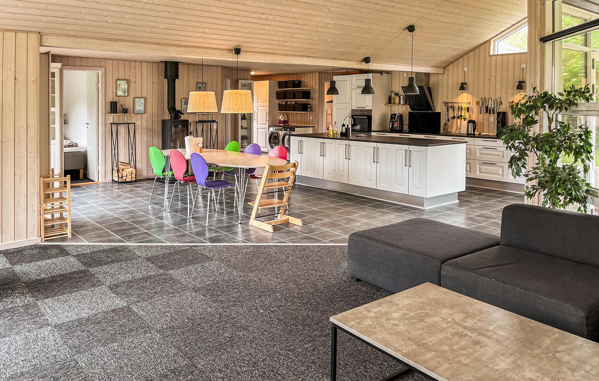 Una cocina moderna con armarios blancos, una isla central y un comedor con sillas coloridas.