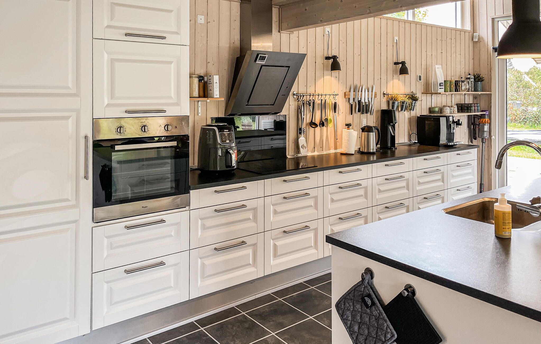 Una cocina moderna con armarios blancos, horno empotrado, cafetera y diversos utensilios de cocina.
