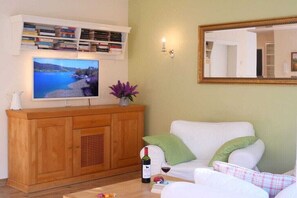 Ein Wohnzimmer mit Fernseher, Holzschrank, weißem Sofa und Spiegel.