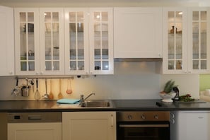 Eine Küche mit weißen Schränken, einer Edelstahl-Spüle, einem Geschirrspüler, einem Backofen und einem kleinen Kühlschrank.