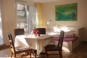 Ein Zimmer mit einem Bett, einem Tisch mit Flasche und Blumen, einem Stuhl, einer Lampe und einem Bild an der Wand.