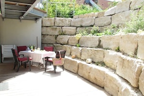 Eine Terrasse mit Tisch und Stühlen, eine steinerne Stützmauer und Blick ins Grüne.