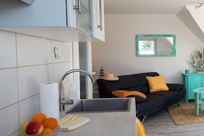 Eine moderne Küche mit Spüle, einem schwarzen Sofa mit gelbem Kissen und einem türkisblauen Schrank.