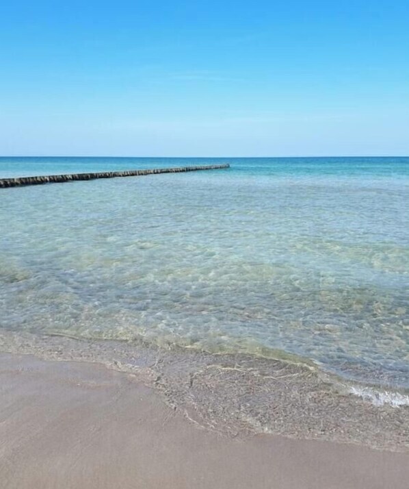 Ein flach abfallender Strand mit klarem Wasser und einer Holzsteige.