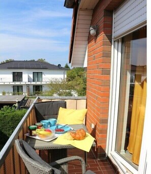 Ein Balkon mit einem Frühstückstisch, einem Stuhl und einem Fenster mit Vorhängen.