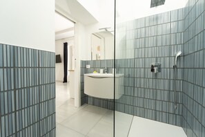 Un bany modern amb una dutxa de vidre, un lavabo blanc i un sòl amb rajoles.
