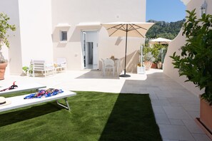 Een terras met een witte tafel, stoelen, een grote parasol en potplanten.