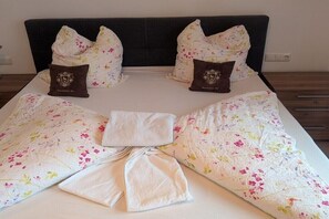 Ein ordentlich bezogenes Bett mit floralem Bettzeug und zwei Zierkissen.