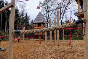 Ein Spielplatz mit einer Seilbrücke, Holz-Klettergerüsten und einem kleinen Turm mit einer Flagge.
