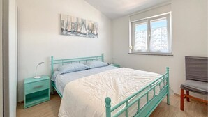 Una camera da letto con un letto, un comodino, una sedia, una finestra con tende a fiori e un dipinto che raffigura un panorama urbano.