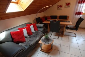 A cozy room with a sofa, a dining table, and chairs. - Holiday apartment with 1 bedroom (Finsterau\/Mauth)