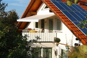 Ein Haus mit geneigtem Dach, einem Balkon mit einer weißen Markise und Solaranlagen auf dem Dach.