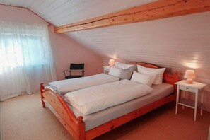 Ein Schlafzimmer mit einem hölzernen Bett, zwei Nachttischen mit Lampen, einem Sessel und einem Fenster mit durchsichtigen Vorhängen.