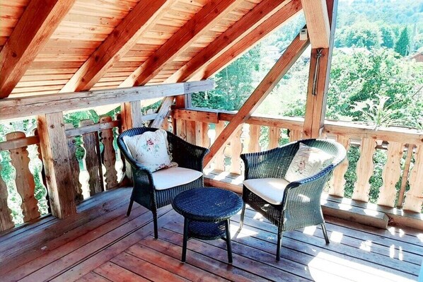 Eine Holzterrasse mit zwei Korbstühlen und einem kleinen runden Tisch mit Blick auf eine bewaldete Landschaft.