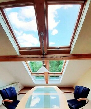Ein Zimmer mit Oberlicht, einem Tisch, zwei Stühlen und einer Pendelleuchte.