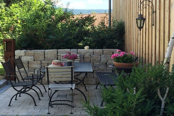 A patio with stone walls, a table, chairs, and potted plants.