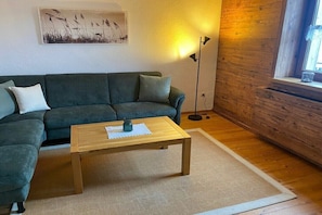 A living room with a green sofa, a wooden coffee table, a floor lamp, and a window with a view.