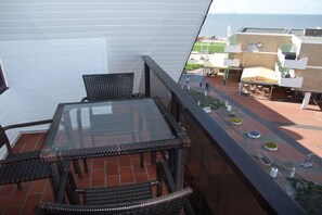 Ein Balkon mit Glastisch und Korbstühlen, mit Blick auf ein Gebäude, an dem das Schild 'Gelateria Italia' zu sehen ist.