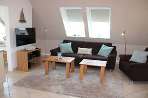 Ein Wohnzimmer mit einer Couch, zwei Beistelltischen, einem Fernseher und einem Bücherregal.
