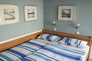 A double bed with striped bedding, a wooden headboard, and three framed pictures on the wall. - Holiday apartment with 2 bedrooms (Cuxhaven)