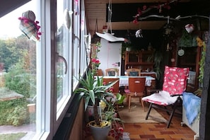 Ein gemütliches Zimmer mit Esstisch, Stühlen, einem roten Sessel mit gemustertem Sitzkissen und einer Topfpflanze.
