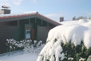 Eine Holzhütte mit geneigtem Dach, umgeben von schneebedecktem Boden und Bäumen.