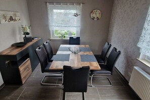 Een eetgedeelte met een houten tafel, zwarte stoelen, een klok aan de muur en een raam met uitzicht.