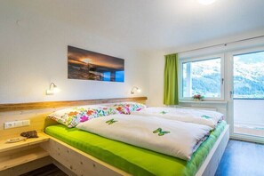 Ein Schlafzimmer mit Bett, einem Fenster mit Vorhängen, einem Wandbild und einem Nachttisch.
