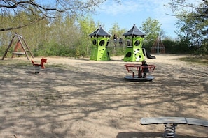 Ein Spielplatz mit Schaukeln, zwei grünen Klettergerüsten und einer Wippe.
