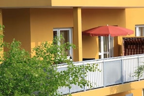 Ein gelbes Gebäude mit Balkon, einem roten Sonnenschirm und einem karierten Markisenvorzelt.