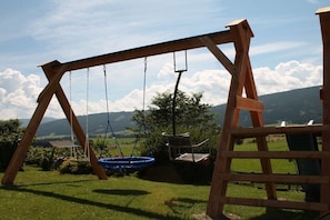 Un’altalena in legno in un’area esterna erbosa, con vista su dolci colline in lontananza.