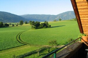 Paesaggio rurale con una baita di legno, un prato verde e montagne sullo sfondo.