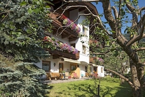 Ein traditionelles Chalet mit Balkon, der mit Blumen geschmückt ist, einer Holzterrasse und einem gepflegten Garten.