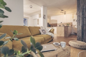 Ein modernes Wohnzimmer mit einer Couch, einem Couchtisch mit einem Laptop und einer Küche im Hintergrund.