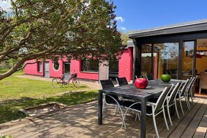 Eine Terrasse mit Tisch und Stühlen, ein Fahrrad und ein rotes Gebäude im Hintergrund.