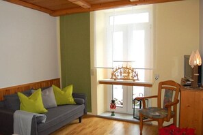 A living room with a sofa, a chair, a wooden cabinet, a television, and a window with a view. - Holiday apartment with 2 bedrooms (Kurort Oberwiesenthal)