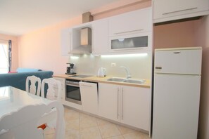 A modern kitchen with white cabinets, a dishwasher, a stove, a microwave, and a refrigerator. - Saranda Point Apartments (Sarande)