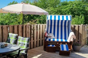 Eine Terrasse mit einem gestreiften Liegestuhl, einem Tisch mit Stühlen und einem Holzzaun.