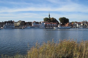 Ein Stadtbild am Wasser mit Gebäuden, einem Kirchturm und Booten auf dem Wasser.