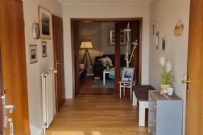 Ein Flur, der in ein Schlafzimmer mit Bett, Nachttisch, Lampe und einer kleinen Pflanze führt.