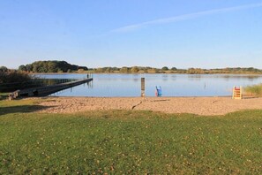 Ein ruhiger See mit Steg, einer Rasenfläche und einer entfernten Hügelkette.