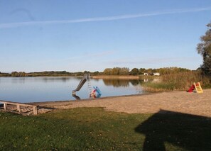 Ein ruhiger See mit einem Spielplatz, der eine Rutsche und eine kleine, rote Konstruktion beinhaltet.