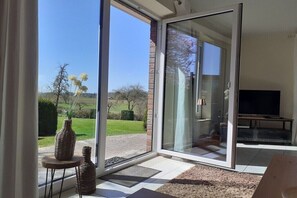 A modern living room with a large sliding glass door leading to a garden, a flat-screen TV, and a small side table with decorative items. - Holiday home in Grebin with swimming pool (Grebin)