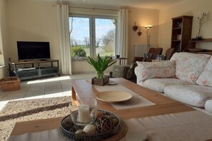 A living room with a sofa, a TV, a plant, and a table with a candle and decorative items. - Holiday home in Grebin with swimming pool (Grebin)