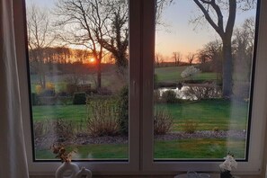A window with a view of a grassy field, trees, and a sunset. - Holiday home in Grebin with swimming pool (Grebin)