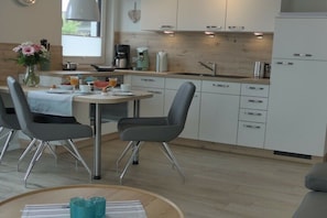 A modern kitchen with white cabinets, a dining table with chairs, and a coffee maker. - Holiday apartment with 1 bedroom (Zingst)